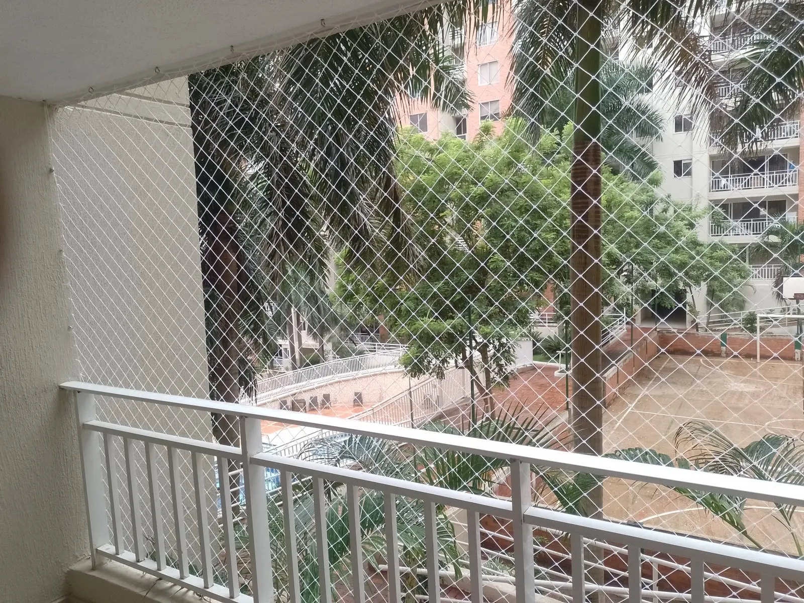 Balcón con baranda blanca y malla de seguridad frente a palmeras